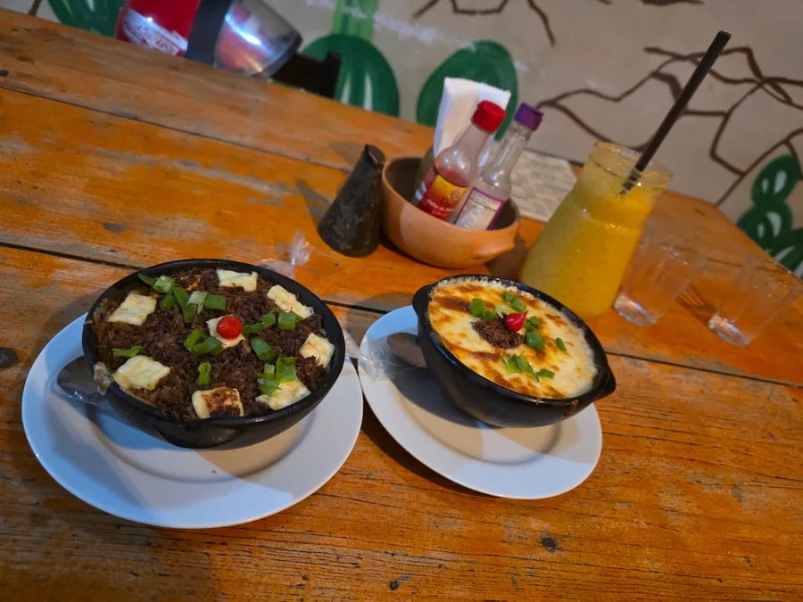 Carne louca gratinada servida em cumbuca de barro, com suco natural ao lado